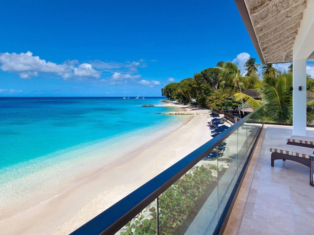A villa terrace looking down a turquoise bay and a white sand beach